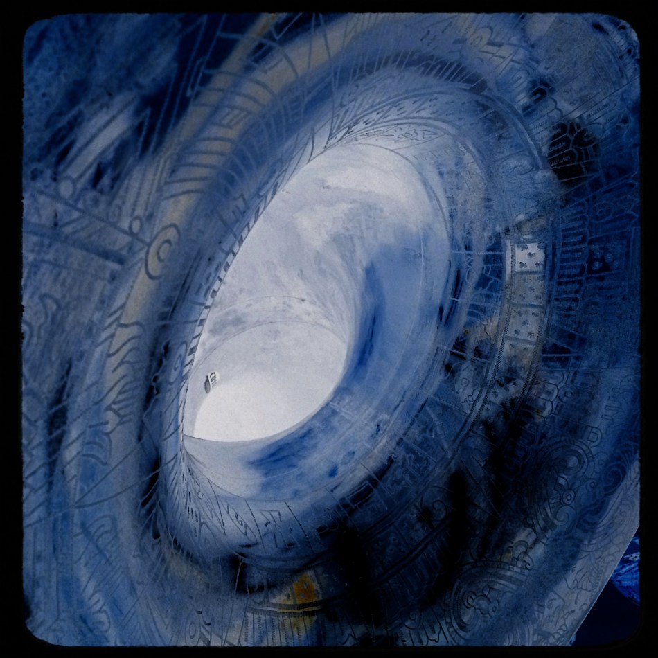 The bell of an engraved sousaphone, converted into a negative and color-boosted to resemble a faux vortex.